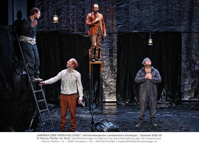 Szene aus Theaterstück Amerika: Zwei Männer stehen auf Leitern, zwei daneben, am Boden liegen ganz viele Stromleitungen