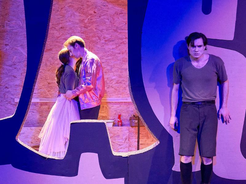 Woyzeck steht vor einer Wand. Seine Frau und deren Geliebter hinter ihm, eng umschlungen.