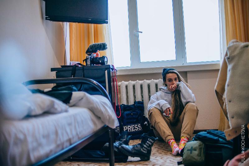 Presse-Journalistin sitzt mit einer Fotoausrüstung inkl. einer gepanzertes Weste am Boden 