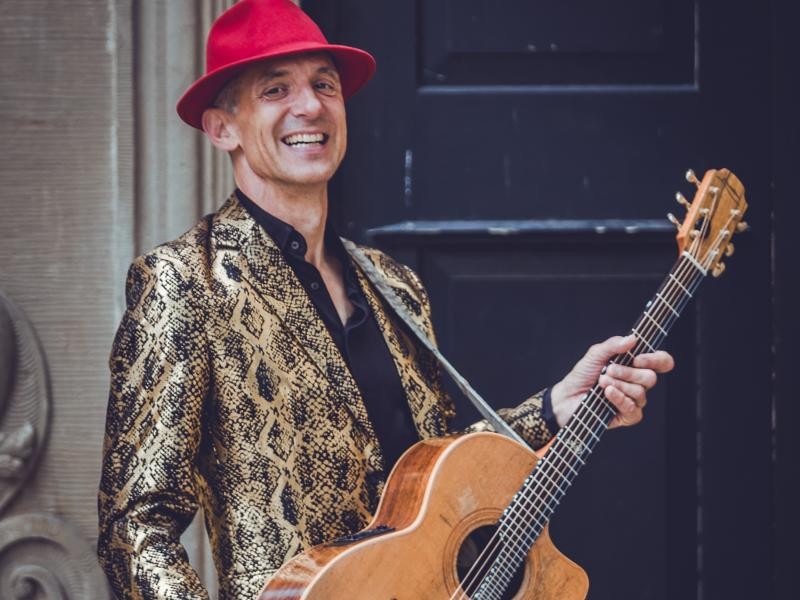 Matthias Waßer Portraitfoto von Matthias Waßer mit Gitarre und rotem Hut