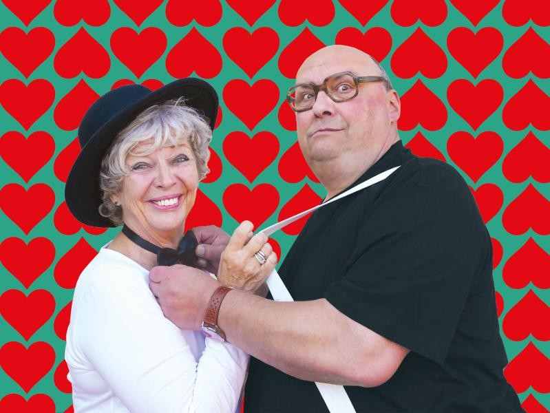 Die Kächeles Herr und Frau Kächele vor einem grünen Hintergrund voll roter Herzen