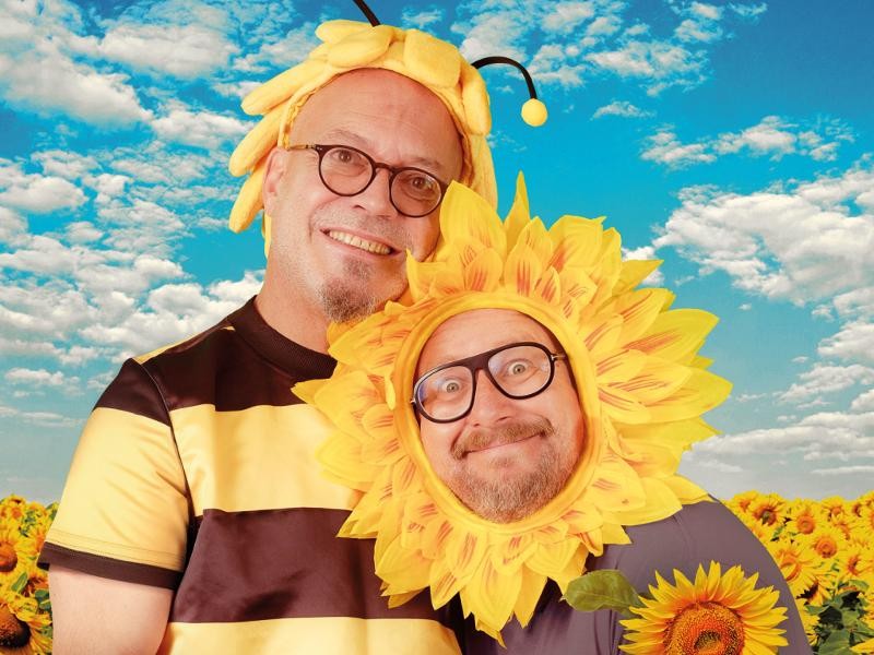 MUNDSTUHL MUNDSTUHL bei blauem Himmel auf einer Sonnenblumenwiese, verkleidet als Biene und Sonnenblume.