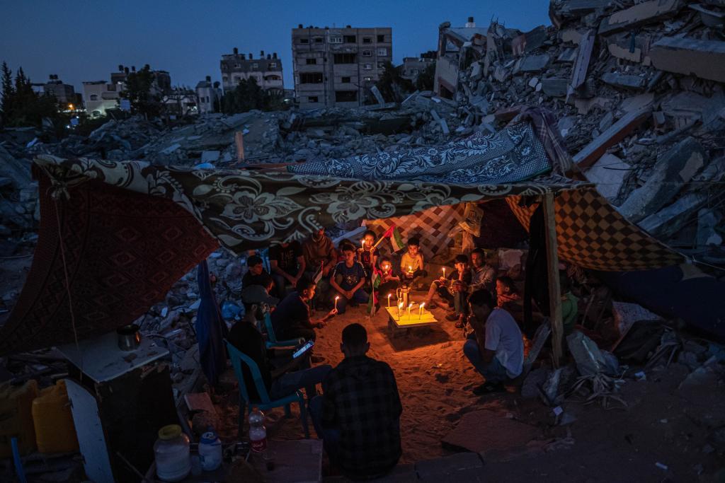 Familie sitzt bei Kerzenschein unter einem Zelt in einer Trümmerlandschaft